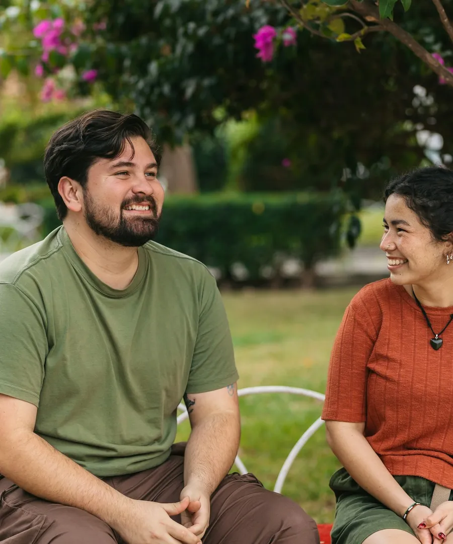 Two people sitting together on a sunlit bench, laughing in conversation.